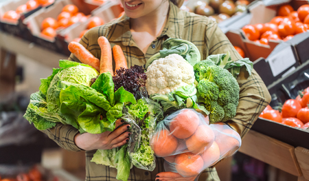 Woman in the supermarket. Organic vegetables close up. Beautiful young woman shopping in a supermarket and buying fresh organic vegetables. The concept of healthy eating. Harvestの写真素材