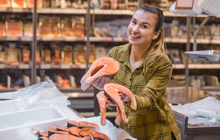 Woman in the supermarket. Beautiful young woman holding a salmon fish in her hands. The concept of healthy eating. Seafoodの写真素材