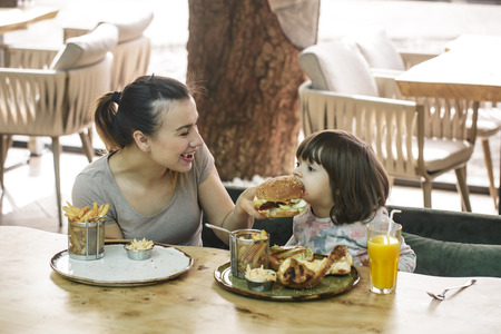 Loving family. Mom with cute daughter eating fast food in a cafe, family and nutrition conceptの写真素材