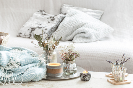 Home decorations in the interior. On the wooden background lies a turquoise blanket and wicker basket with a vase of flowers and candles. Concept of comfortの写真素材