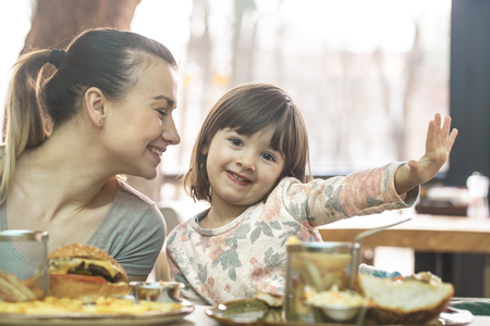 Loving family. Mom with cute daughter eating fast food in a cafe, family and nutrition conceptの写真素材