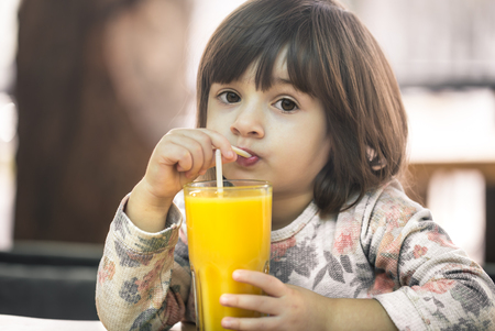 Little cute girl in a cafe is drinking orange juice, baby food conceptの写真素材