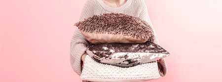 Hands of woman holding modern three pillows for sofa, pink wall background in trend, minimalism...