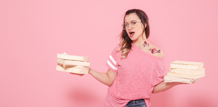 Horizontal portrait of a girl with a stack of books, on a pink background, lifestyle and education conceptの写真素材