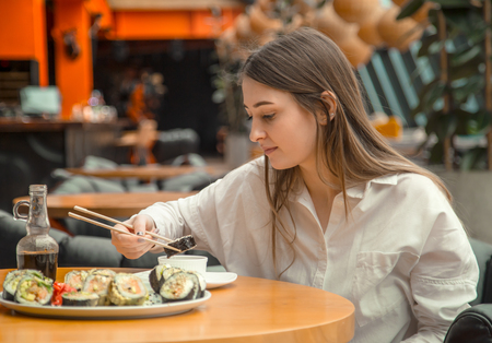 Young Woman eating and enjoying fresh sushi in luxury restaurant. Female client holding food sticks and eating oriental meal on lunch. Concept of food.の写真素材