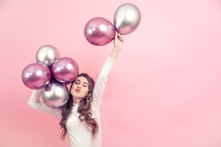 Young girl with beautiful balls on a colored pink background, dressed in a white dress, the concept of women's day and holidayの写真素材