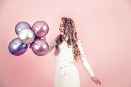 Young girl with beautiful balls on a colored pink background, dressed in a white dress, the concept of women's day and holidayの写真素材