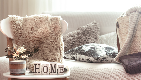 Chic interior for a house. Candles, a vase with flowers with wooden letters of the home on wooden white chair. Sofa and wicker basket with cushions in the background. Home decoration.の写真素材