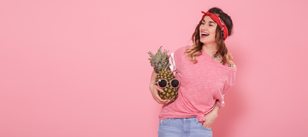 Beautiful young girl in pink t-shirt with decal water tattoo sticker, smiling with pineapple on pink background. Place for text. Advertising conceptの写真素材