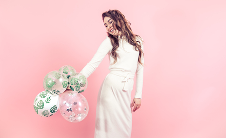 Young girl with balloons in a tropical print on a colored pink background, dressed in a beautiful white dress, the concept of women's day and holidayの写真素材