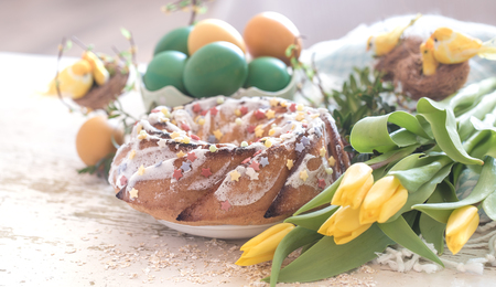 Still life with Easter cake and colorful eggs in a saucer, and yellow tulips on a light background, the concept of the holidayの写真素材