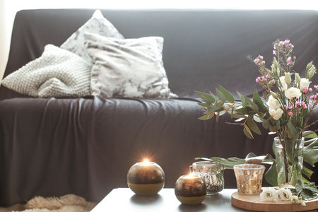 Cozy home interior with elements of decor in the living room with a black sofa and a vase of flowers and lighted candles on a small table.の写真素材