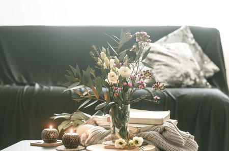 Cozy home interior with elements of decor in the living room with a black sofa and a vase of flowers and lighted candles on a small table.の写真素材