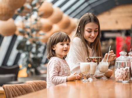 Happy young women mother with children sitting at the table and drinking a milkshake in a restaurant or cafe. In Leisure and communication with children restaurant. The concept of familyの写真素材