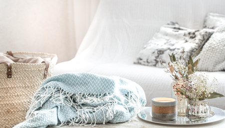 Home decorations in the interior. On the wooden background lies a turquoise blanket and wicker basket with a vase of flowers and candles. Concept of comfortの写真素材