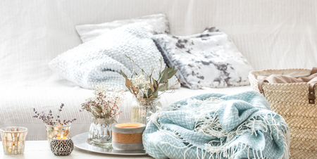 Home decorations in the interior. On the wooden background lies a turquoise blanket and wicker basket with a vase of flowers and candles. Concept of comfortの写真素材