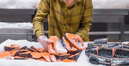 Woman in the supermarket. Beautiful young woman holding a salmon fish in her hands. The concept of healthy eating. Seafoodの写真素材