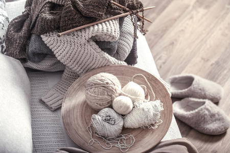 Vintage wooden knitting needles and threads on a cozy sofa with pillows and Slippers nearby. Still life photo. The concept of comfortの写真素材