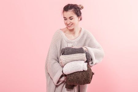 Woman in knitted sweater holds many knitted sweaters on pink background. Knitting, Cleaning.の写真素材