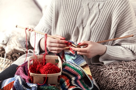 wooden spokes and red yarn in the hands of a woman on a cozy sofa . Still life photo. The concept of comfortの写真素材