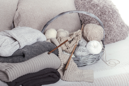 Vintage wooden knitting needles and threads in a large basket on a cozy sofa with sweaters. Still life photo. The concept of comfortの写真素材