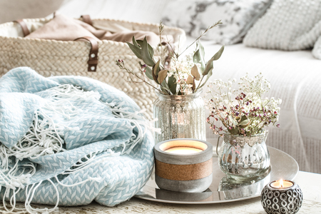 Home decorations in the interior. On the wooden background lies a turquoise blanket and wicker basket with a vase of flowers and candles. Concept of comfortの写真素材