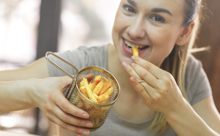 Young woman in cafe eats french fries, fast food conceptの写真素材