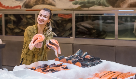 Woman in the supermarket. Beautiful young woman holding a salmon fish in her hands. The concept of healthy eating. Seafoodの写真素材