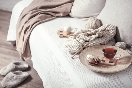 Vintage wooden spokes and yarn on a cozy sofa with a sweater and a Cup of tea . Still life photo. The concept of comfortの写真素材