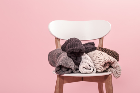 White chair with a stack of knitted sweaters on a pink background. Autumn Winter concept.の写真素材