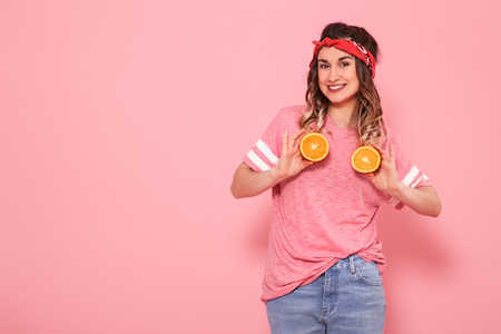 Horizontal portrait of hipster girl in stylish clothes with oranges in their hands, healthy food, on pink background, lifestyle conceptの写真素材