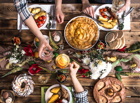 Traditional Easter celebration, Easter holiday party. Holiday friends or family at the festive table with rabbit meat, vegetables, pies, eggs, top view. Friends hands eating and drinking together.の写真素材