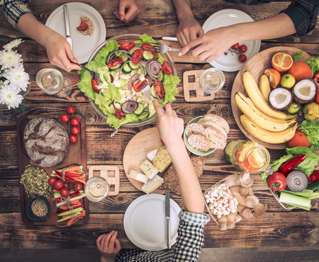 Enjoying dinner with my friends. Top view of a group of people dining together, sitting at a rustic wooden table, the concept of celebration and healthy home-cooked foodの写真素材