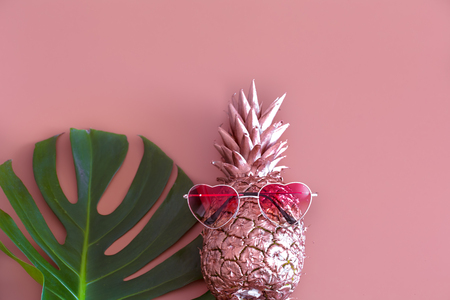 Golden pineapple with a tropical leaf and glasses in shape of heart on colored pastel background, the concept of summer and creativityの写真素材