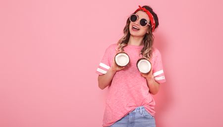 Horizontal portrait of hipster girl in stylish clothes with sunglasses, coconuts in her hands, on a pink background, lifestyle conceptの写真素材