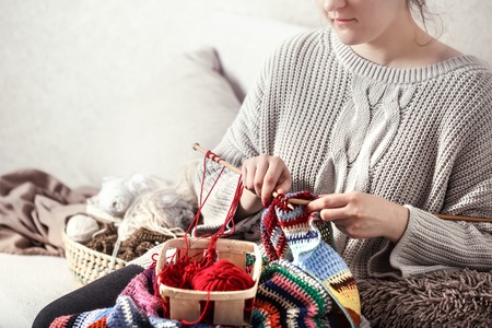 wooden spokes and red yarn in the hands of a woman on a cozy sofa . Still life photo. The concept of comfortの写真素材
