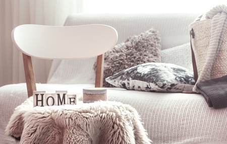 Chic interior for a house. Candles, a vase with flowers with wooden letters of the home on wooden white chair. Sofa and wicker basket with cushions in the background. Home decoration.の写真素材
