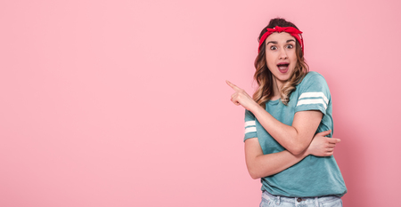 Horizontal portrait of Caucasian girl hipster shows finger to side in stylish clothes with a bright T-shirt and a red bandage, isolated on a pink background, lifestyle conceptの写真素材
