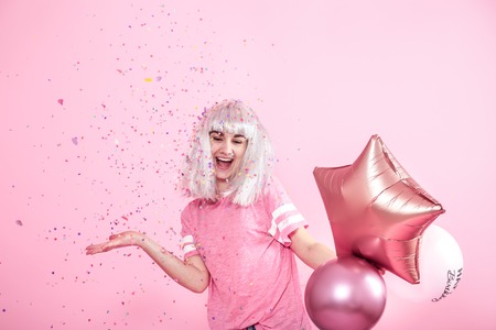 Funny Girl with silver hair gives a smile and emotion on pink background. Young woman or teen girl with balloons and confetti. Concept of holiday and party.の写真素材