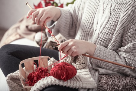 wooden spokes and red yarn in the hands of a woman on a cozy sofa . Still life photo. The concept of comfortの写真素材