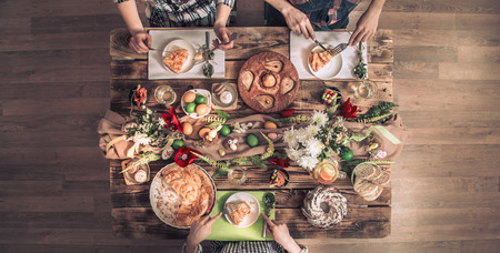 Traditional Easter celebration, Easter holiday party. Holiday friends or family at the festive table with rabbit meat, vegetables, pies, eggs, top view. Friends hands eating and drinking together.の写真素材