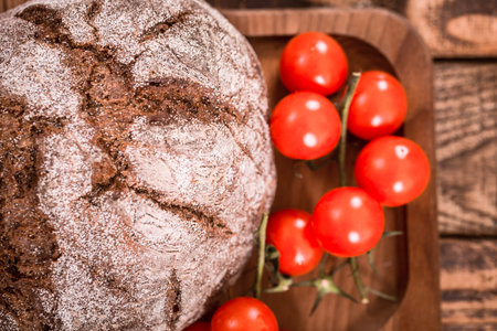 Fresh dark round bread on a wooden plate with small tomatoes closeup, food concept