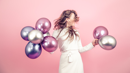 Young girl with beautiful balls on a colored pink background, dressed in a white dress, the concept of women's day and holidayの写真素材