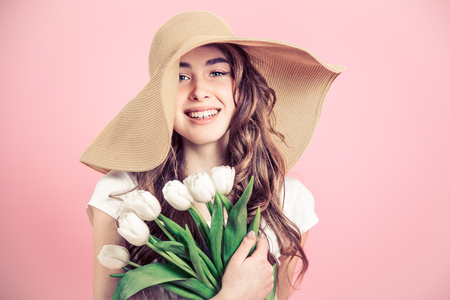 Young beautiful girl in a big summer hat and white tulips on a colored background, the concept of women's day and holidayの写真素材