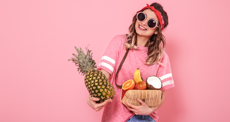 Horizontal portrait of hipster girl in stylish clothes with sunglasses, with healthy food, fruits, on pink background, lifestyle conceptの写真素材