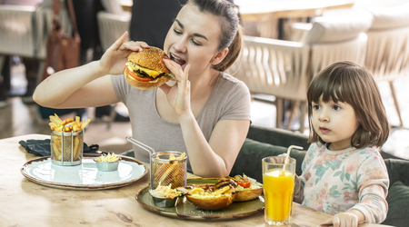 Loving family. Mom with cute daughter eating fast food in a cafe, family and nutrition conceptの写真素材