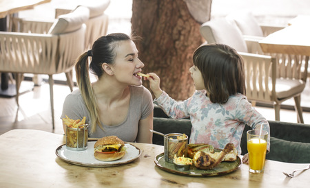 Loving family. Mom with cute daughter eating fast food in a cafe, family and nutrition conceptの写真素材