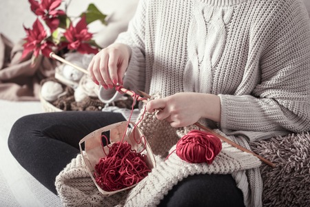 wooden spokes and red yarn in the hands of a woman on a cozy sofa . Still life photo. The concept of comfortの写真素材