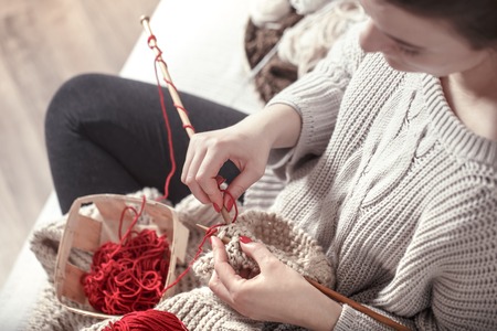 wooden spokes and red yarn in the hands of a woman on a cozy sofa . Still life photo. The concept of comfortの写真素材
