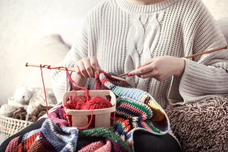 wooden spokes and red yarn in the hands of a woman on a cozy sofa . Still life photo. The concept of comfortの写真素材
